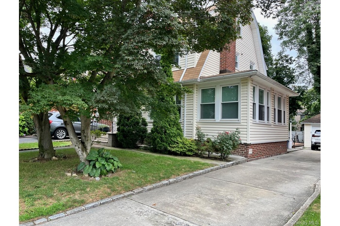 View of front of property featuring a gambrel roof, an outdoor structure, a front lawn, and a detached garage
