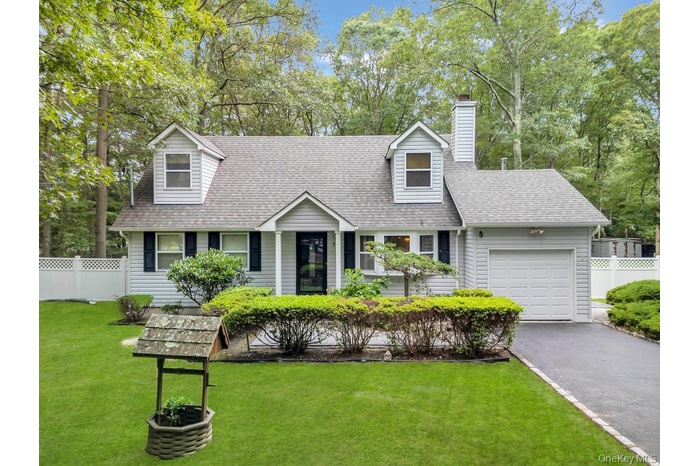 Cape cod home featuring an attached garage, a shingled roof, asphalt driveway, a chimney, and view of scattered trees