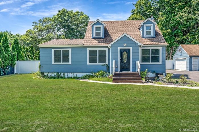 New england style home featuring a shingled roof, a garage, an outbuilding, asphalt driveway, and a chimney
