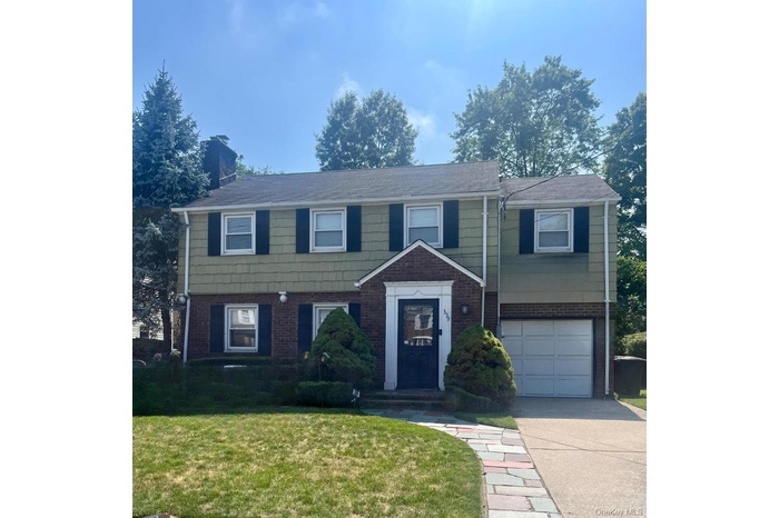 View of front of house featuring a garage, driveway, brick siding, a front yard, and a chimney