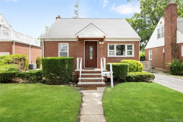 View of front of home with brick siding, a front lawn, and roof with shingles
