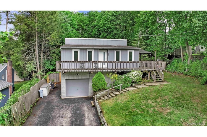 View of front of house featuring stairway, driveway, an attached garage, a deck, and brick siding