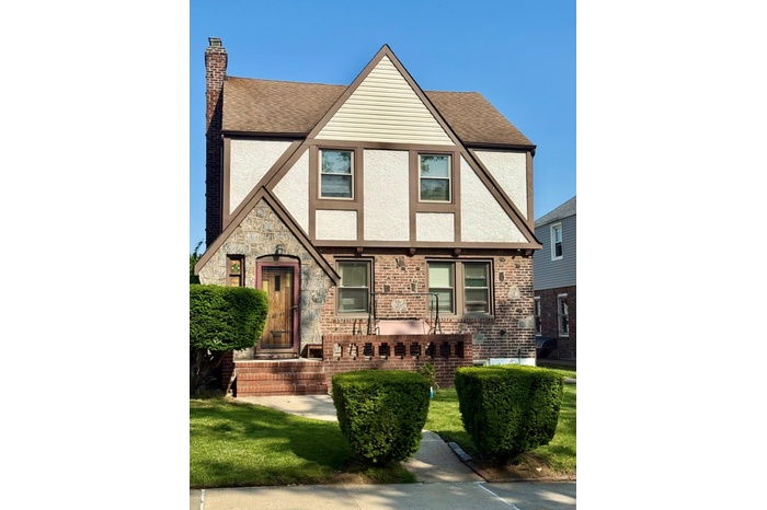Tudor house with roof with shingles, stucco siding, a chimney, and a front lawn