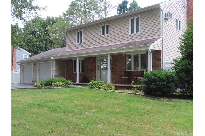 Traditional-style house with a garage, covered porch, a front yard, and brick siding