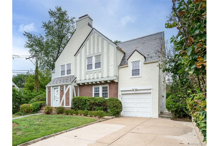 English style home with a high end roof, a garage, stucco siding, and brick siding