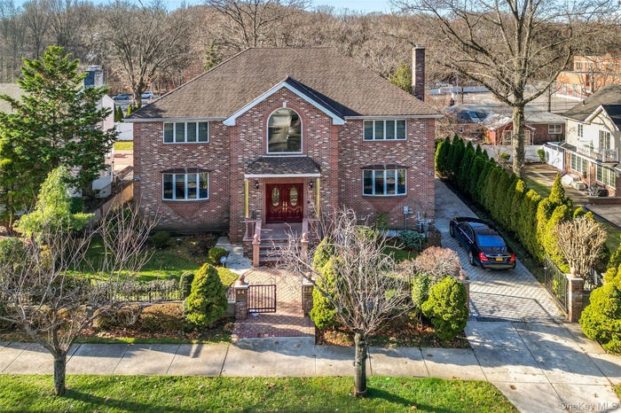 Traditional-style house with a fenced front yard, a chimney, a shingled roof, brick siding, and a gate