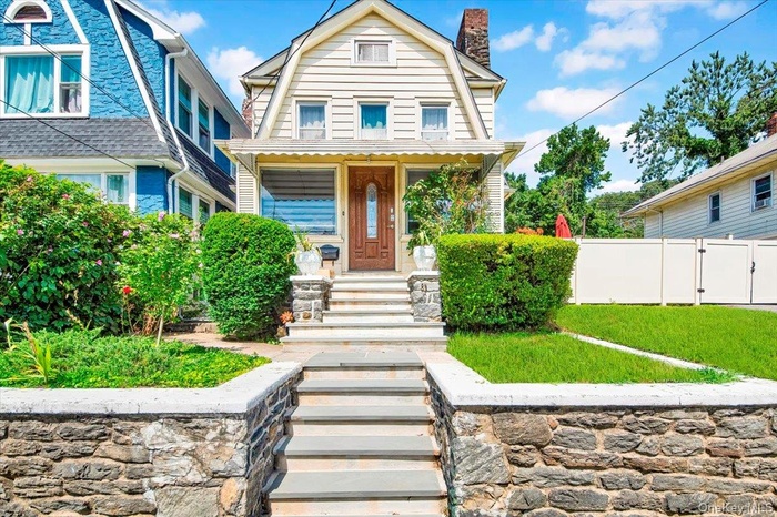 Colonial inspired home with a chimney, a gate, a gambrel roof, and covered porch
