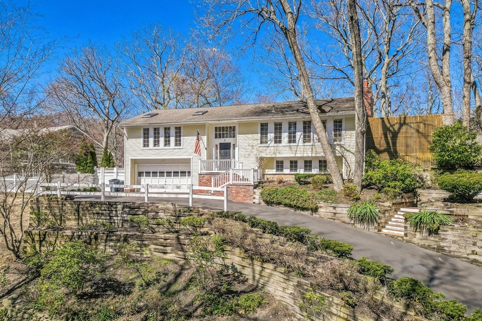 Raised ranch with an attached garage, fence, stairway, concrete driveway, and roof with shingles