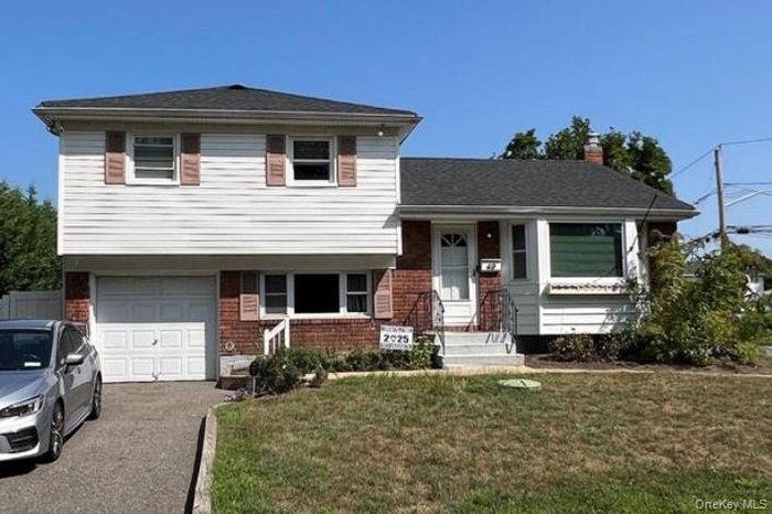 Tri-level home featuring brick siding, a front lawn, a garage, a porch, and a chimney