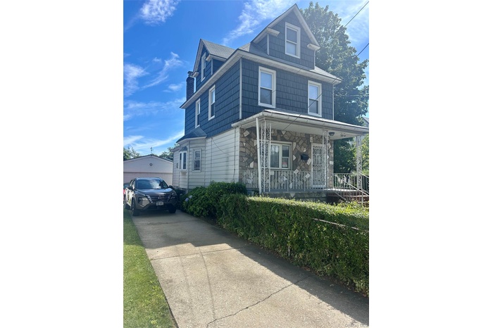 American foursquare style home featuring a porch, driveway, and stone siding