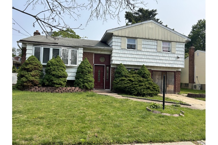 Tri-level home featuring a front lawn, brick siding, and a chimney
