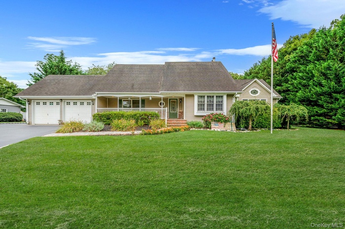 View of front of property featuring covered porch, driveway, a garage, roof with shingles, and a front lawn