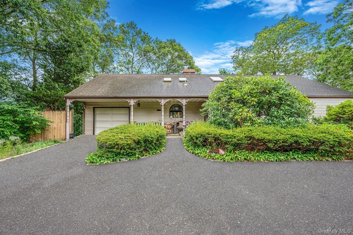 View of front of property with driveway, roof with shingles, a porch, an attached garage, and a chimney