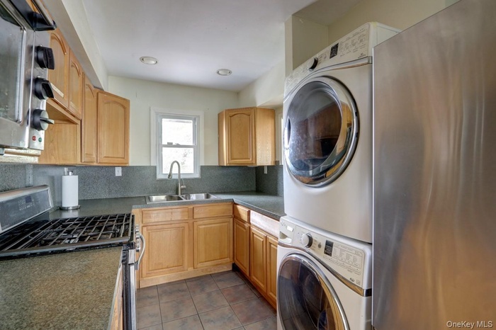 Kitchen featuring stacked washing machine and dryer, stainless steel gas range oven, dark countertops, tasteful backsplash, and dark tile patterned fl