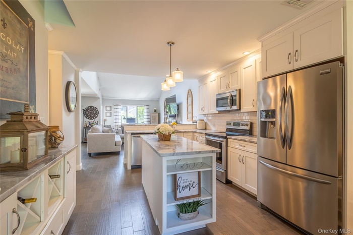 Kitchen with appliances with stainless steel finishes, open floor plan, open shelves, tasteful backsplash, and decorative light fixtures