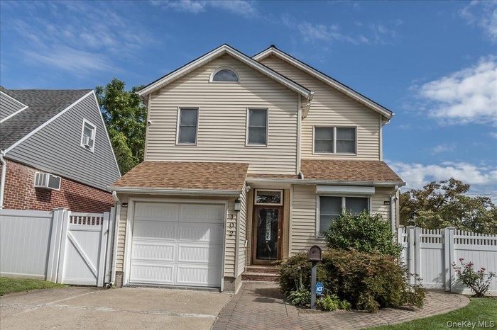 Traditional-style home with a gate, a garage, driveway, and a shingled roof