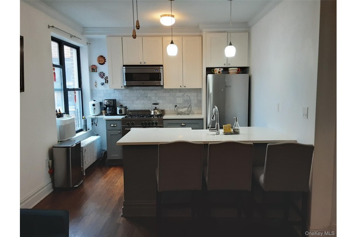 Kitchen featuring tasteful backsplash, stainless steel appliances, ornamental molding, light countertops, and decorative light fixtures