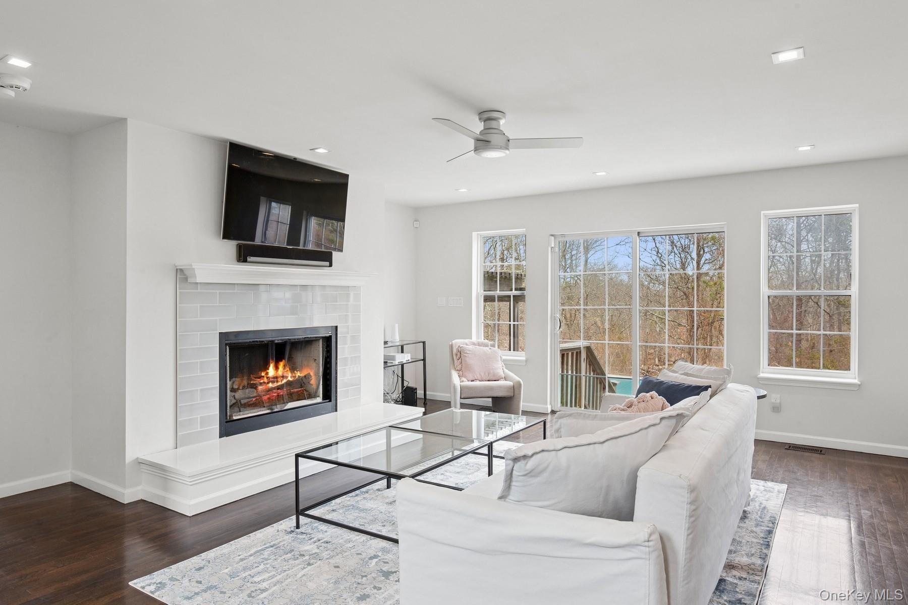 Living room with ceiling fan, baseboards, wood finished floors, and a warm lit fireplace