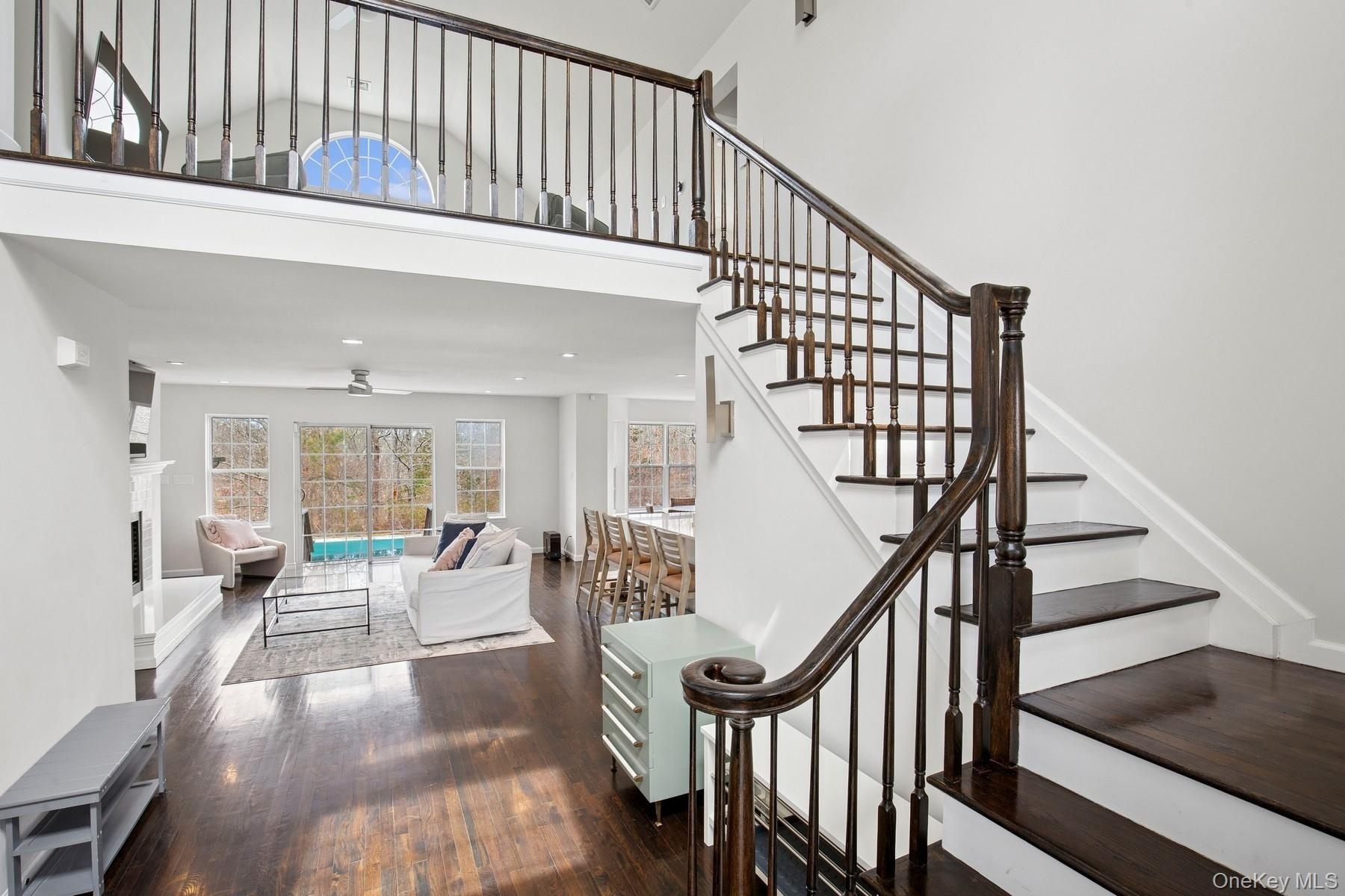 Stairs with a fireplace, a ceiling fan, recessed lighting, a high ceiling, and wood-type flooring