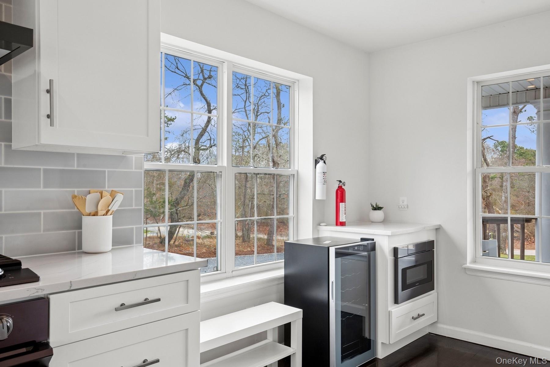 Kitchen featuring wine cooler, stainless steel microwave, backsplash, and white cabinets