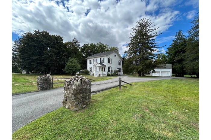 View of front of home with a front yard, driveway, view of wooded area, and an outdoor structure