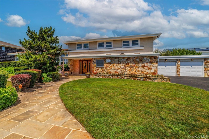 View of front of property featuring a front lawn, stone siding, a garage, and asphalt driveway
