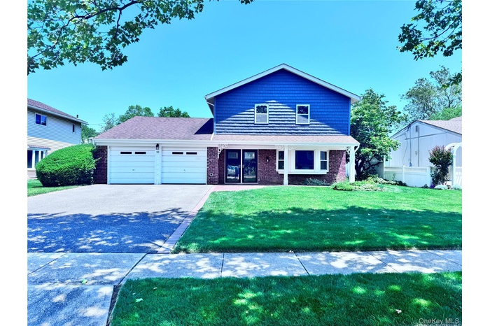 Traditional-style house featuring an attached garage, driveway, a front lawn, brick siding, and a porch