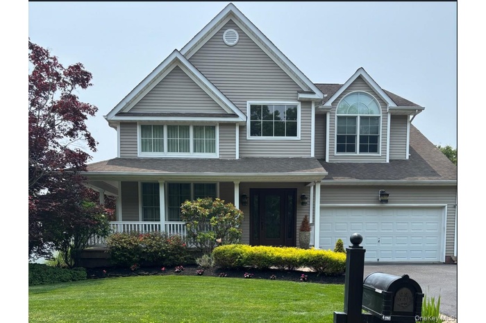 View of front of property with driveway, a porch, a front yard, a shingled roof, and an attached garage