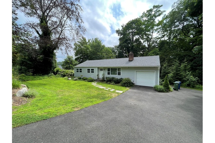 Single story home with a garage, a chimney, a front yard, driveway, and roof with shingles
