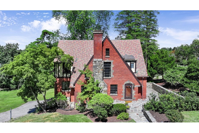Tudor-style house featuring brick siding, a chimney, a high end roof, a front lawn, and stone siding