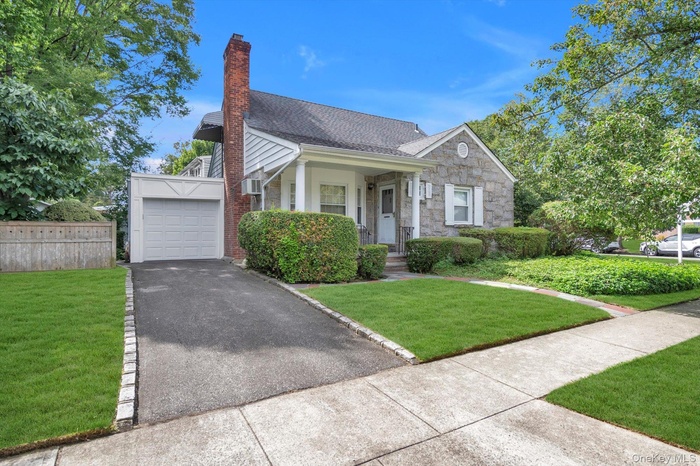 View of front of house featuring a shingled roof, a porch, a chimney, driveway, and a garage