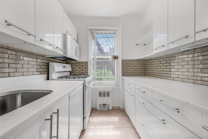 Kitchen with white cabinetry, gas range gas stove, light tile patterned floors, and backsplash