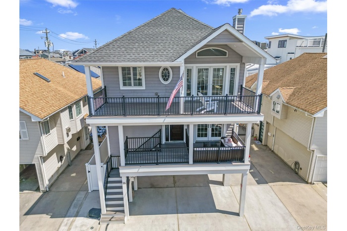 Back of house with a shingled roof, a chimney, stairway, and a balcony