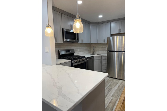 Kitchen featuring tasteful backsplash, appliances with stainless steel finishes, decorative light fixtures, light stone countertops, and gray cabinets