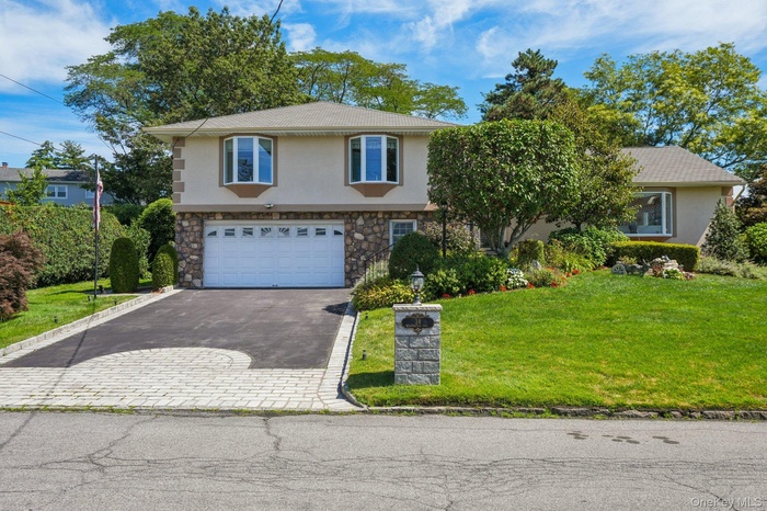View of front of home with stone siding, a front lawn, a garage, driveway, and stucco siding