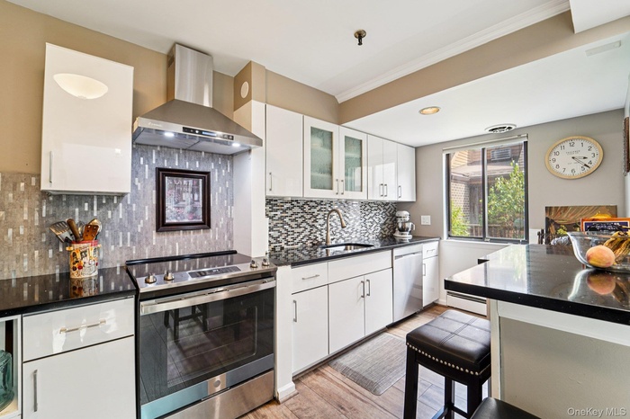 Kitchen featuring appliances with stainless steel finishes, white cabinetry, wall chimney exhaust hood, decorative backsplash,