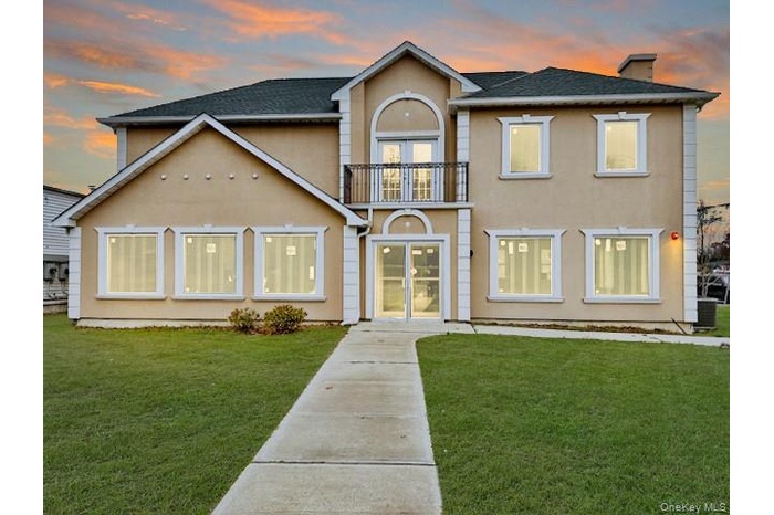 View of front of property with stucco siding, a balcony, a chimney, french doors, and a yard