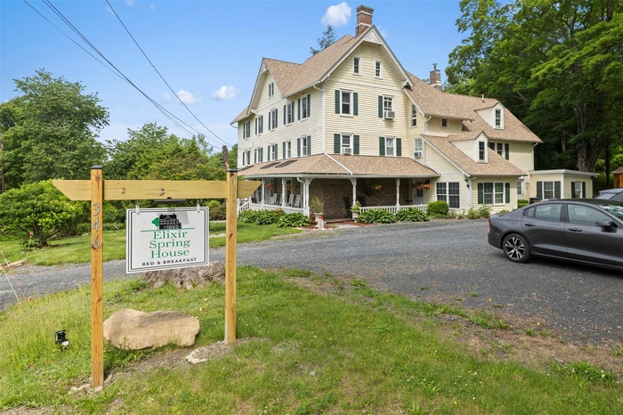 View of front of home featuring a chimney, covered porch, and roof with shingles