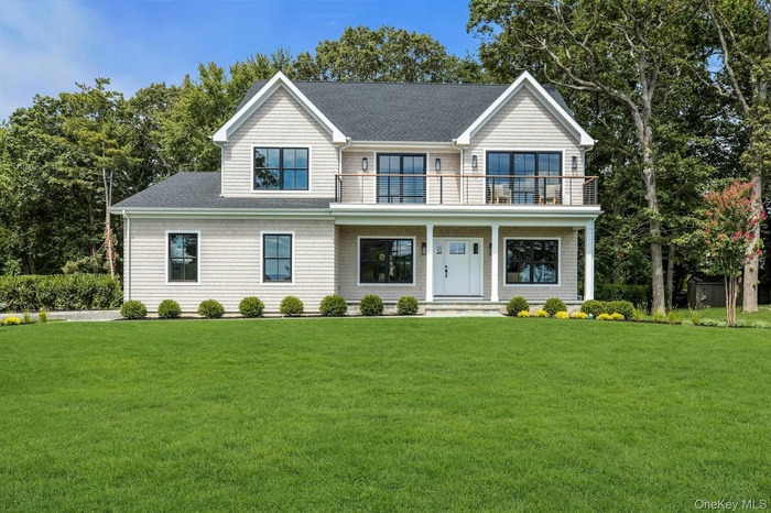View of front of home with a front yard, a shingled roof, a porch, a balcony, and view of wooded area