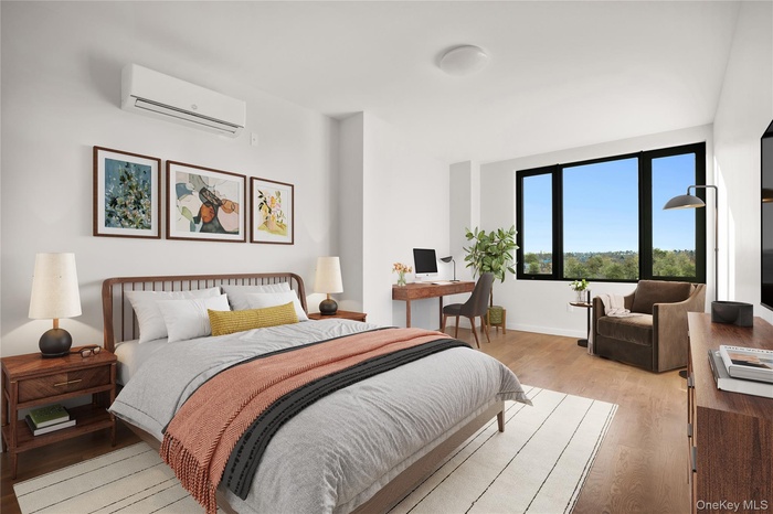 Bedroom with a wall mounted AC, light wood-type flooring, an office area, and baseboards