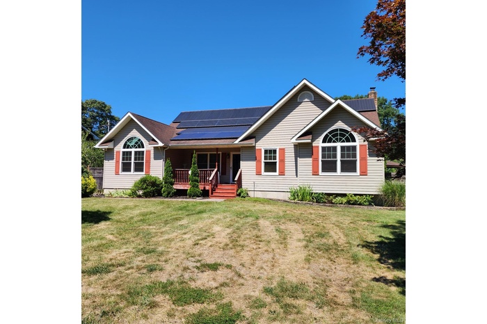 Single story home with roof mounted solar panels, a porch, a chimney, and a front lawn