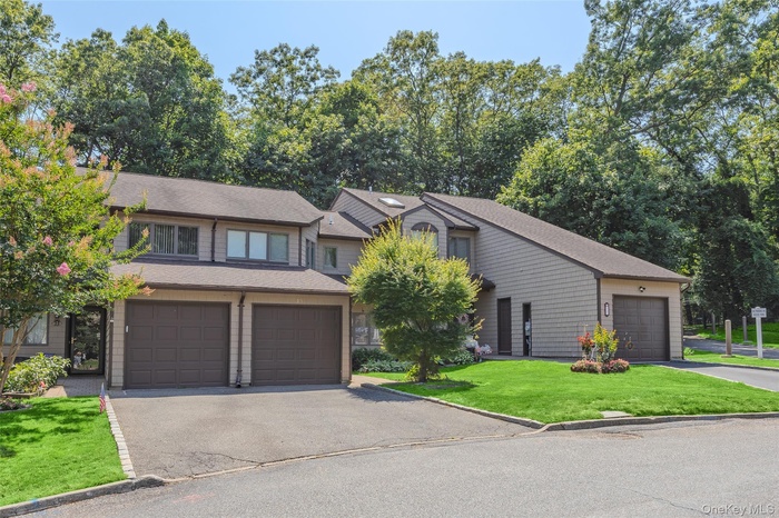 View of front of house featuring a front lawn, a shingled roof, asphalt driveway, and view of wooded area