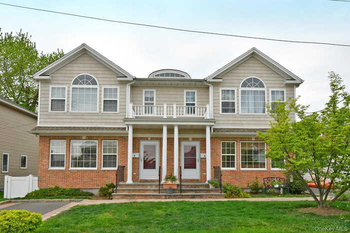 View of front facade featuring a front lawn, brick siding, a balcony, and a porch