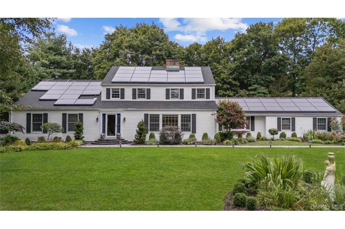 View of front facade with solar panels, a front yard, roof with shingles, and view of scattered trees