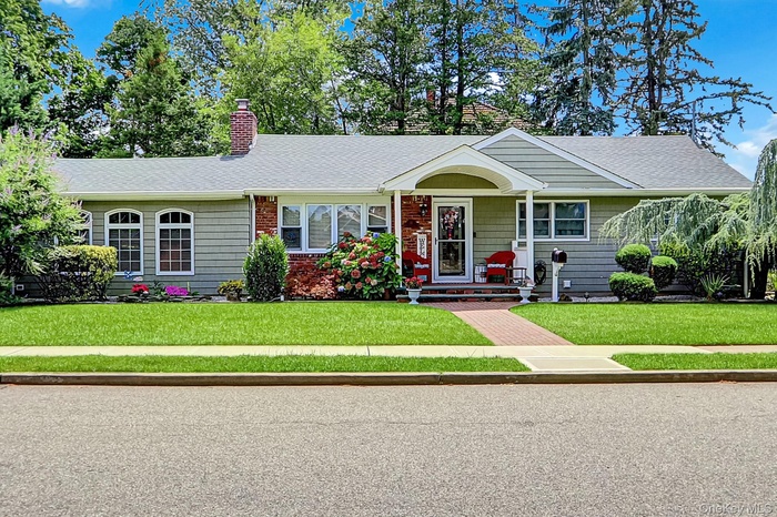 Ranch-style home featuring a front lawn, a shingled roof, a chimney, and a porch