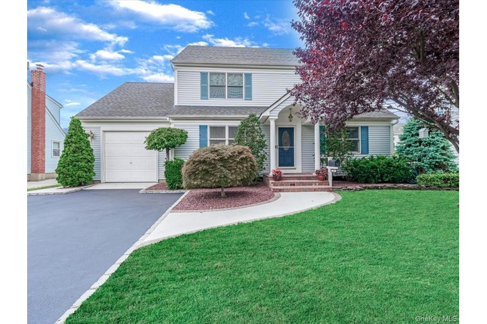Traditional-style home with an attached garage, roof with shingles, asphalt driveway, and a front lawn