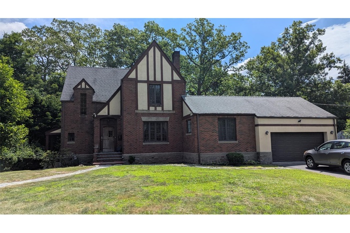 Tudor house with an attached garage, a chimney, brick siding, and asphalt driveway