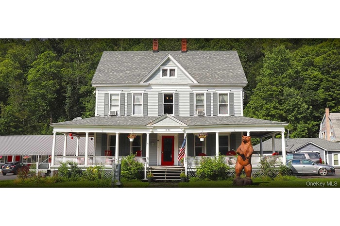 View of front facade with covered porch, roof with shingles, and a view of trees