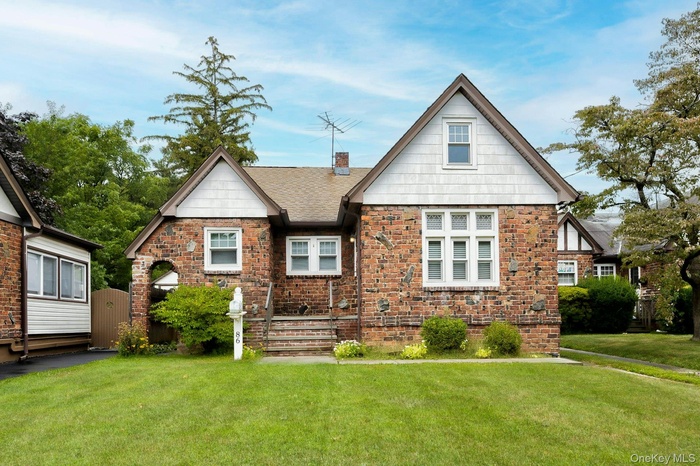 Tudor home featuring a chimney, a front yard, a gate, and stone siding