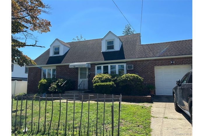 Cape cod house featuring an attached garage, roof with shingles, brick siding, and a fenced front yard